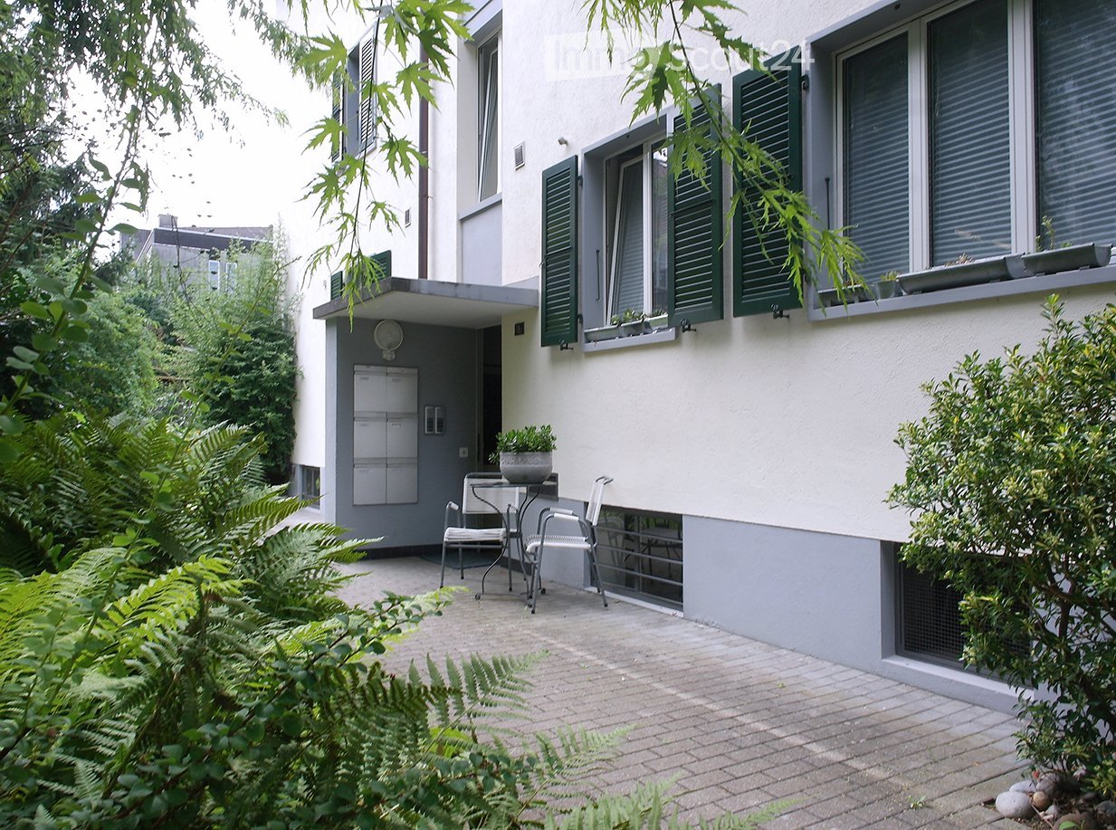 Exterior view with brick floor patio, mailbox, green shutter windows, a table with chairs, and potted plants.
