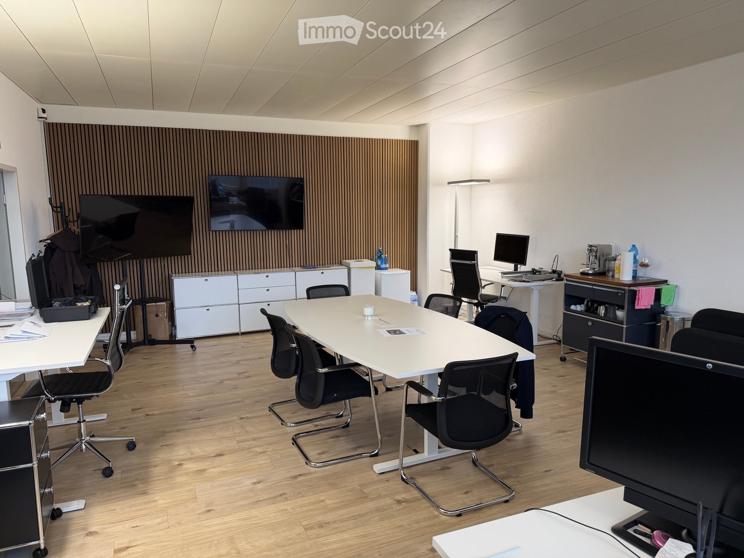 Office space with a large conference table, chairs, multiple screens, and cabinets.
