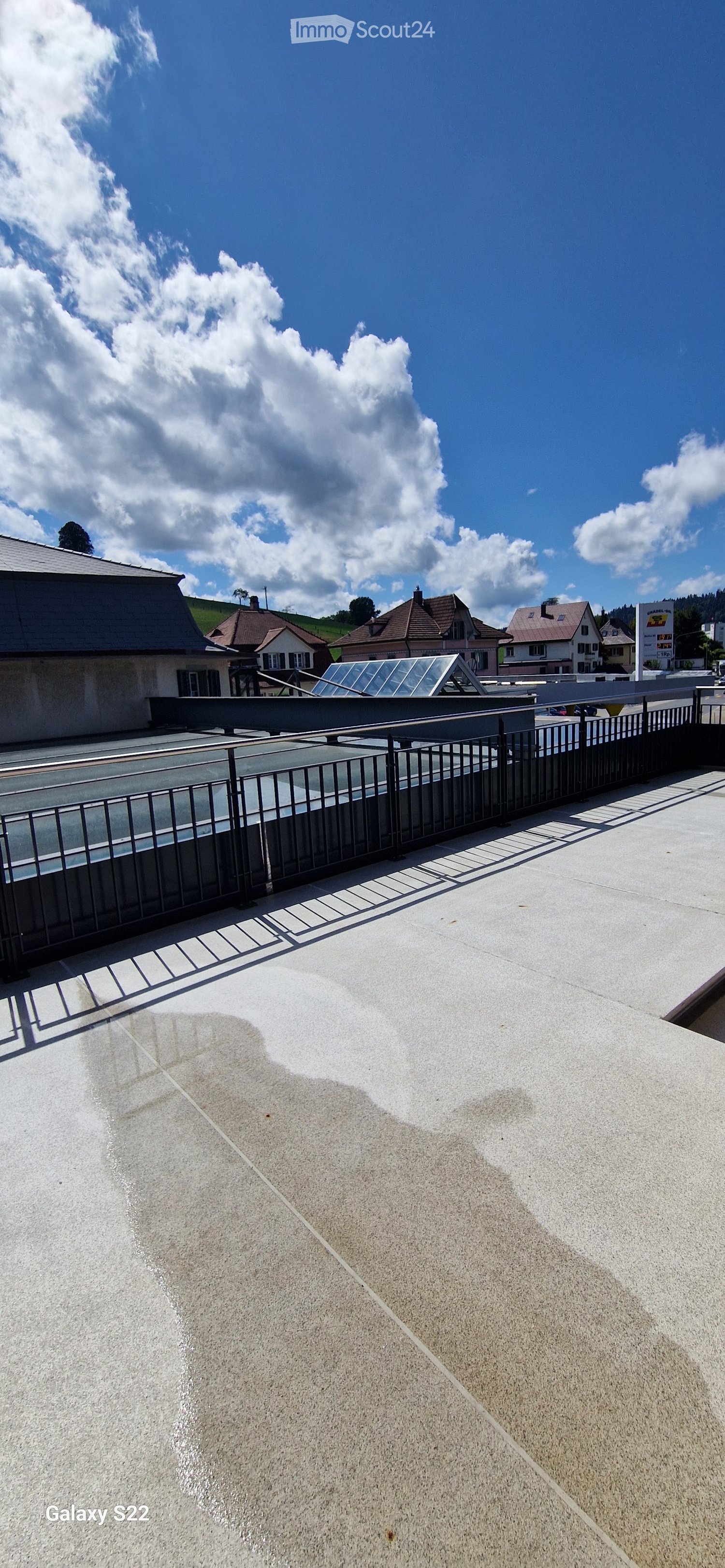 Roof terrace with concrete surface, metal railing, and a glass roof structure in the background.