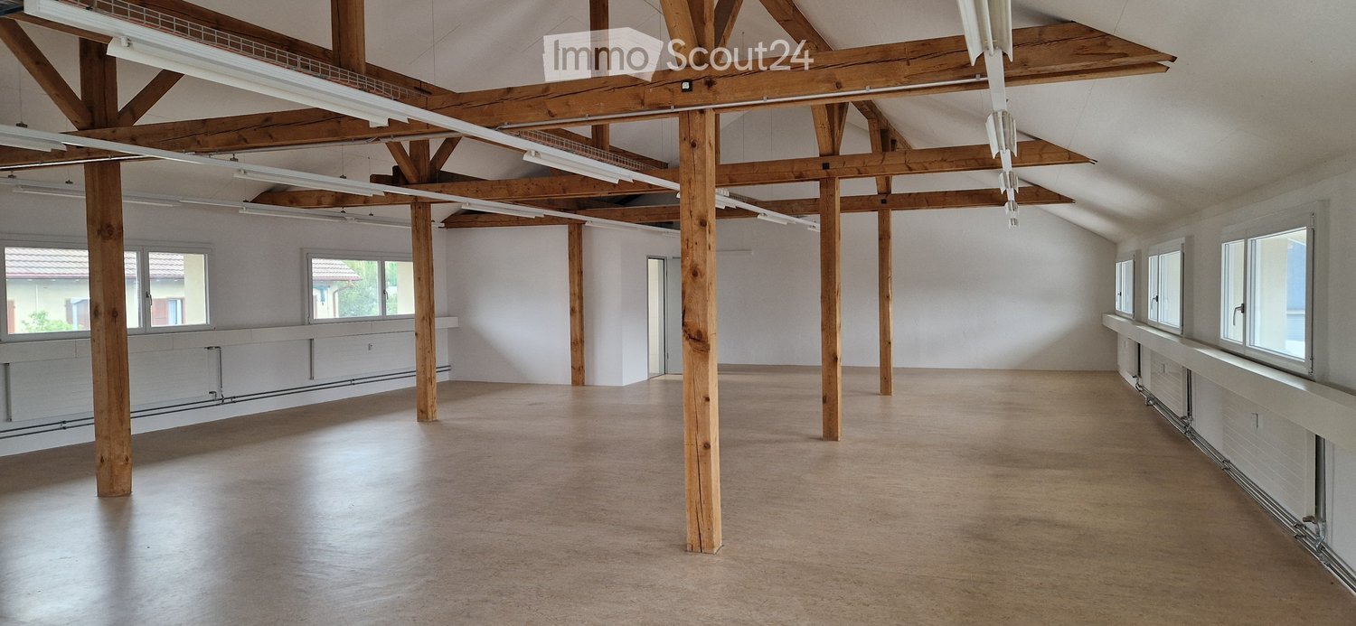 Empty room with wooden beams, polished wooden floor, large windows, and white walls.