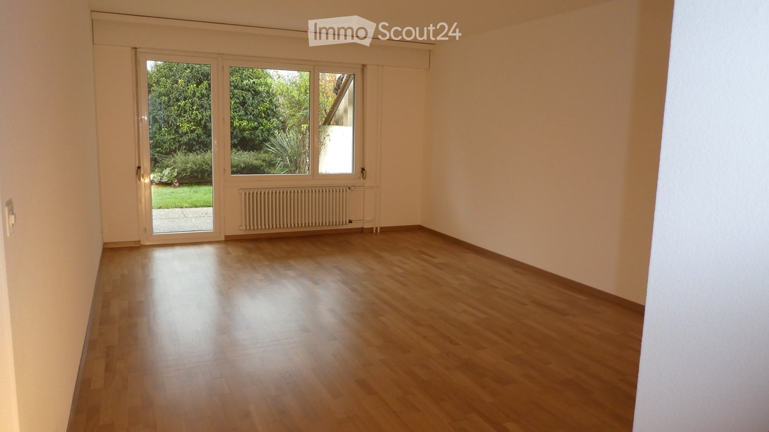 Wooden floor, sliding door leading to balcony, white walls, white radiator, window, no furniture