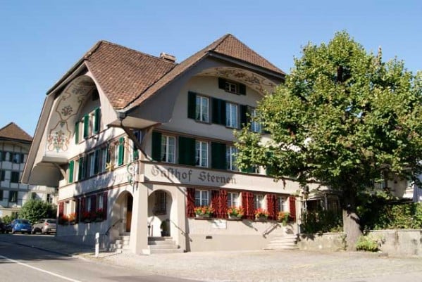 Traditional Swiss building with a brown roof, green shutters, and red window boxes with flowers.