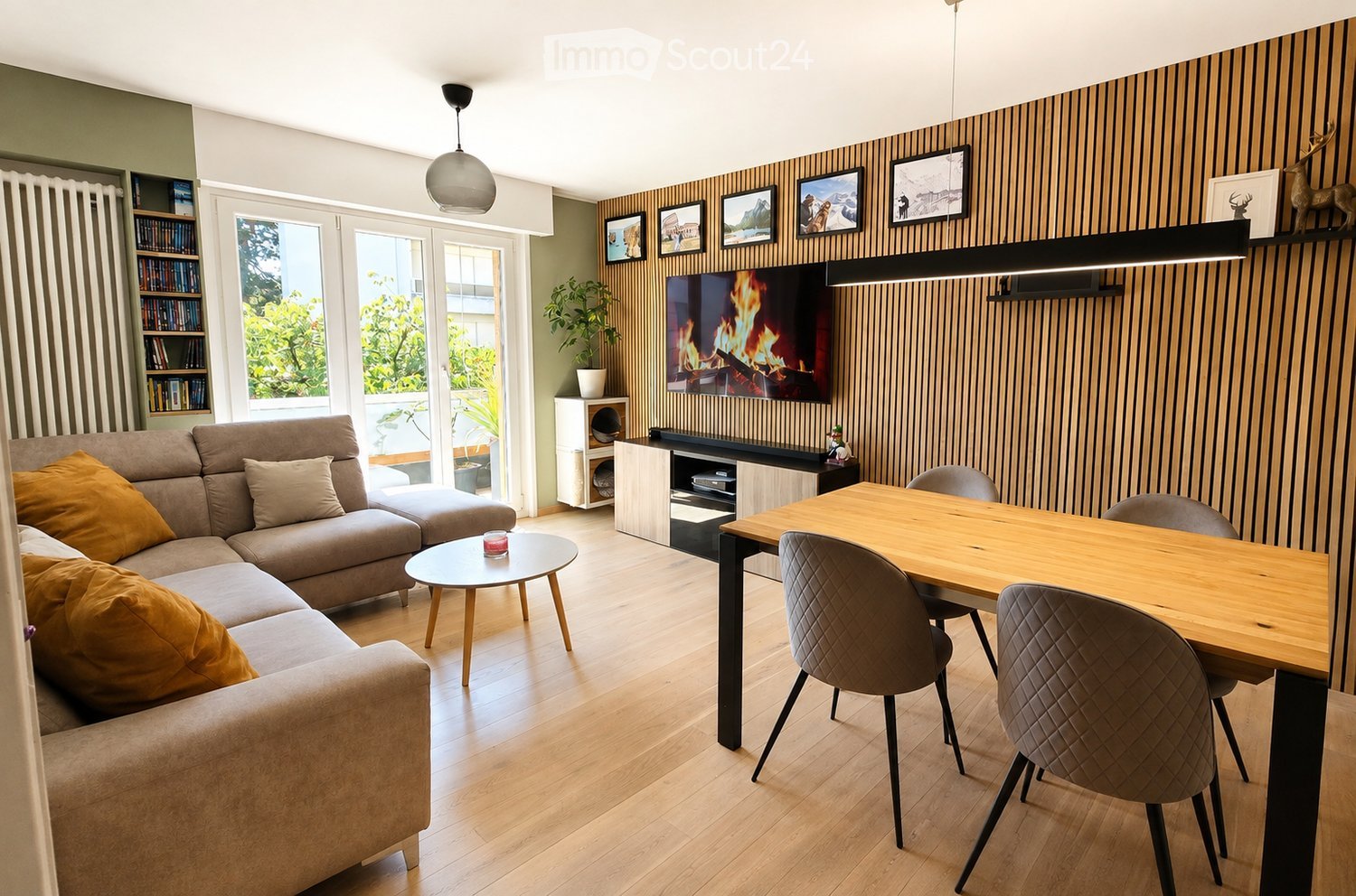 Modern living room with a sectional sofa, coffee table, dining table with chairs, bookshelf, TV, pendant lights, and decorative items.