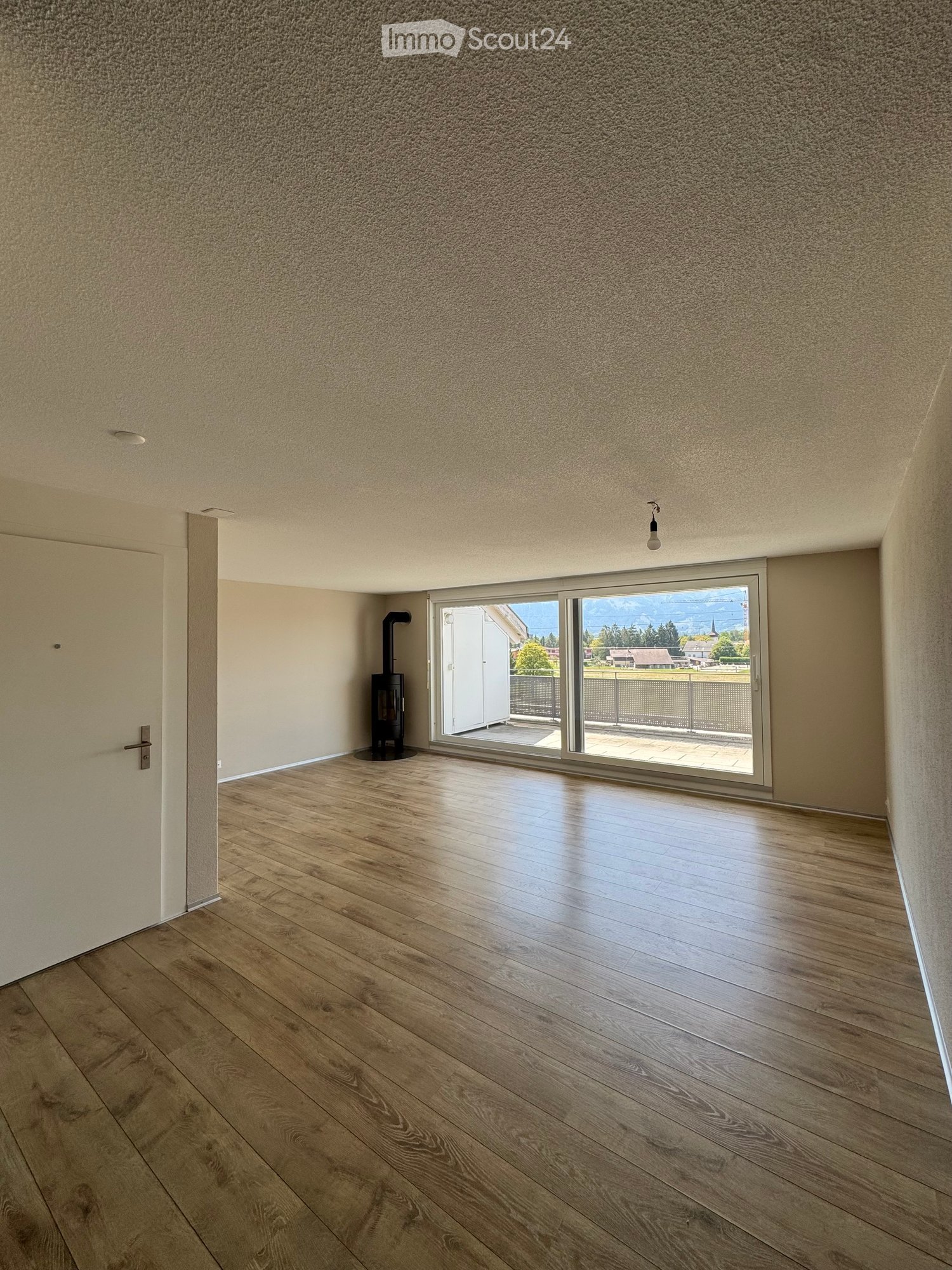Empty room with wooden flooring, white walls, and a sliding glass door leading to a balcony with a scenic mountain view.