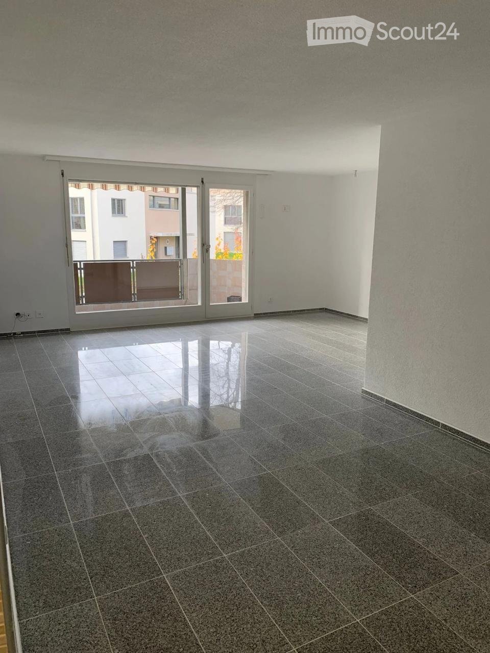 Empty room with dark tiled floor and large sliding glass doors leading to a balcony.