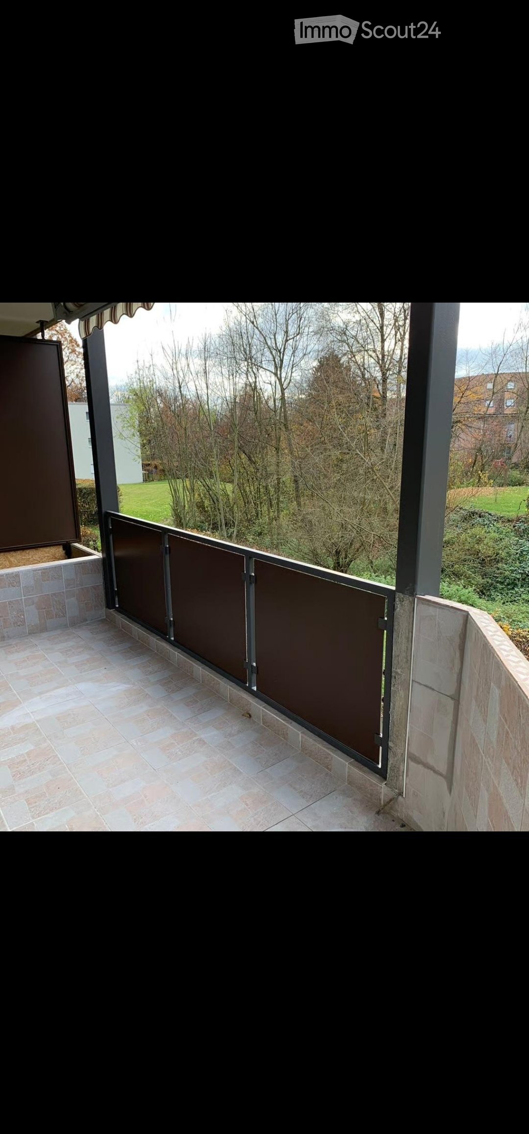 Balcony with tiled floor, metal railing, and view of a green landscape with trees and a house in the background.
