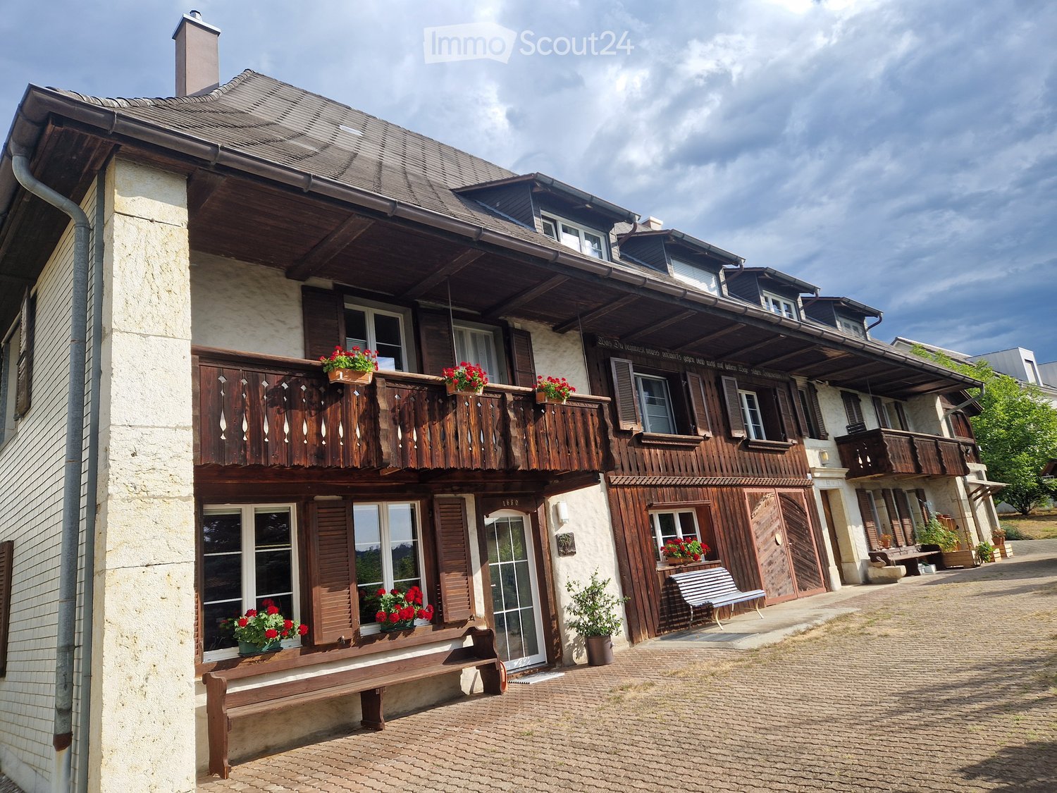 Two-story traditional house with wooden balconies, stone facade, and flower boxes on windowsills.