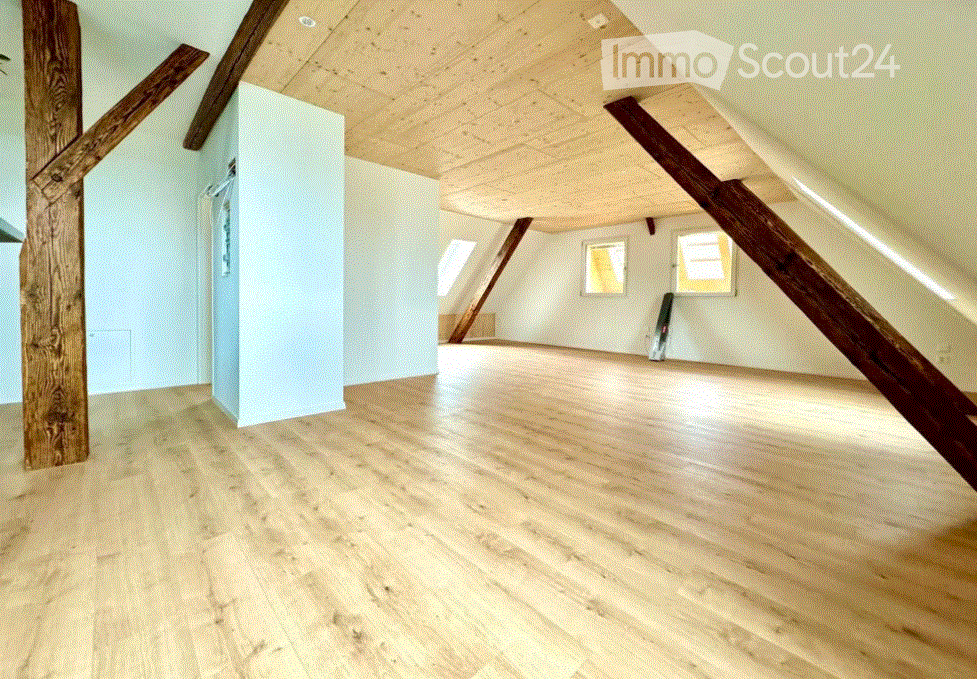 Empty attic space with wooden floors, exposed wooden beams, and skylight windows.