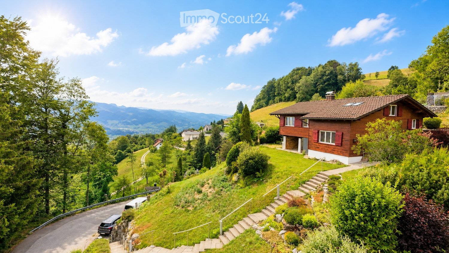 A two-story wooden house with red shutters and a tiled roof, situated on a hillside with a scenic mountain view in the background.