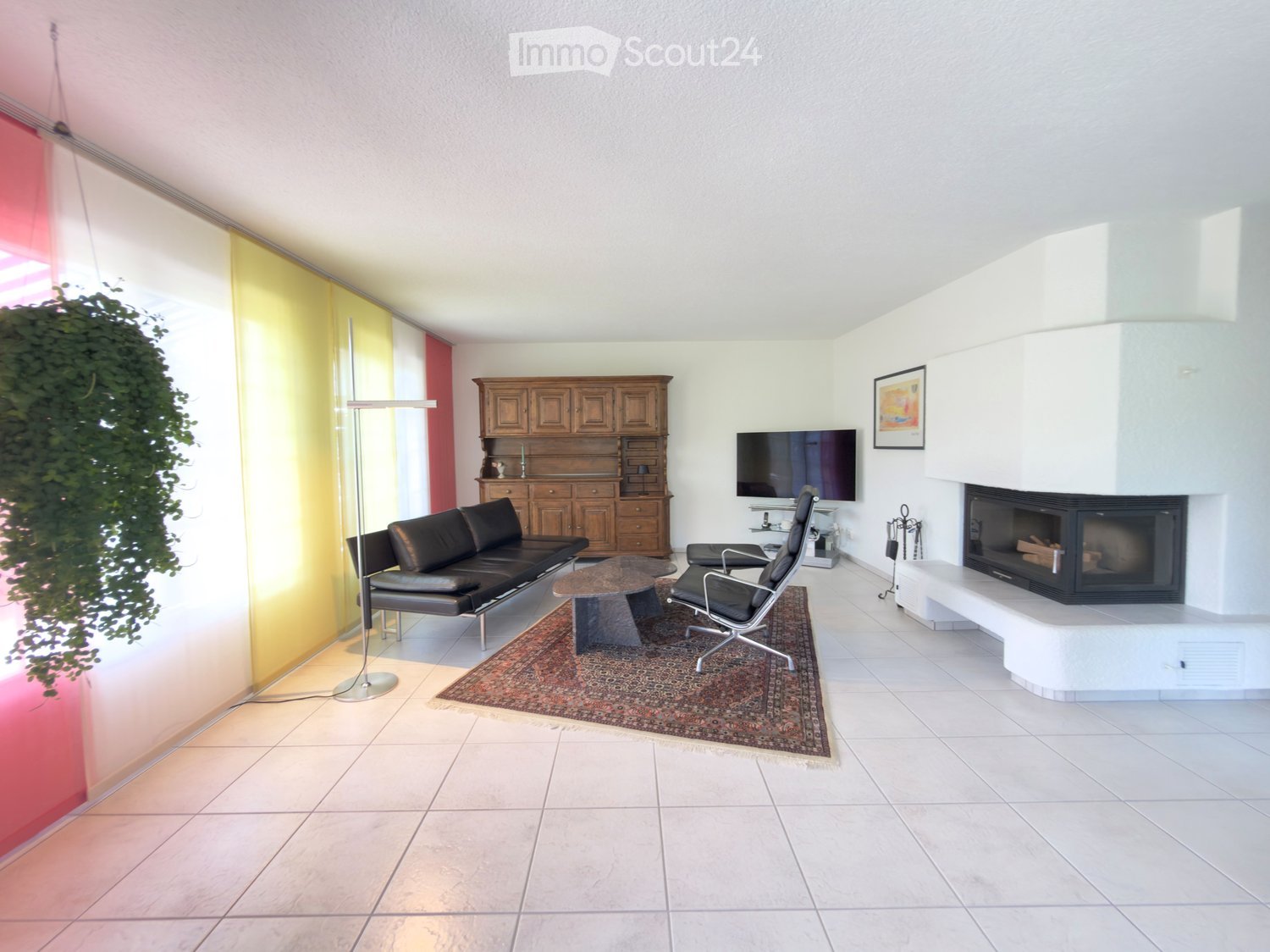 Modern living room with white tiled flooring, a black leather sofa, a coffee table, a fireplace, a TV, and a wooden cabinet.