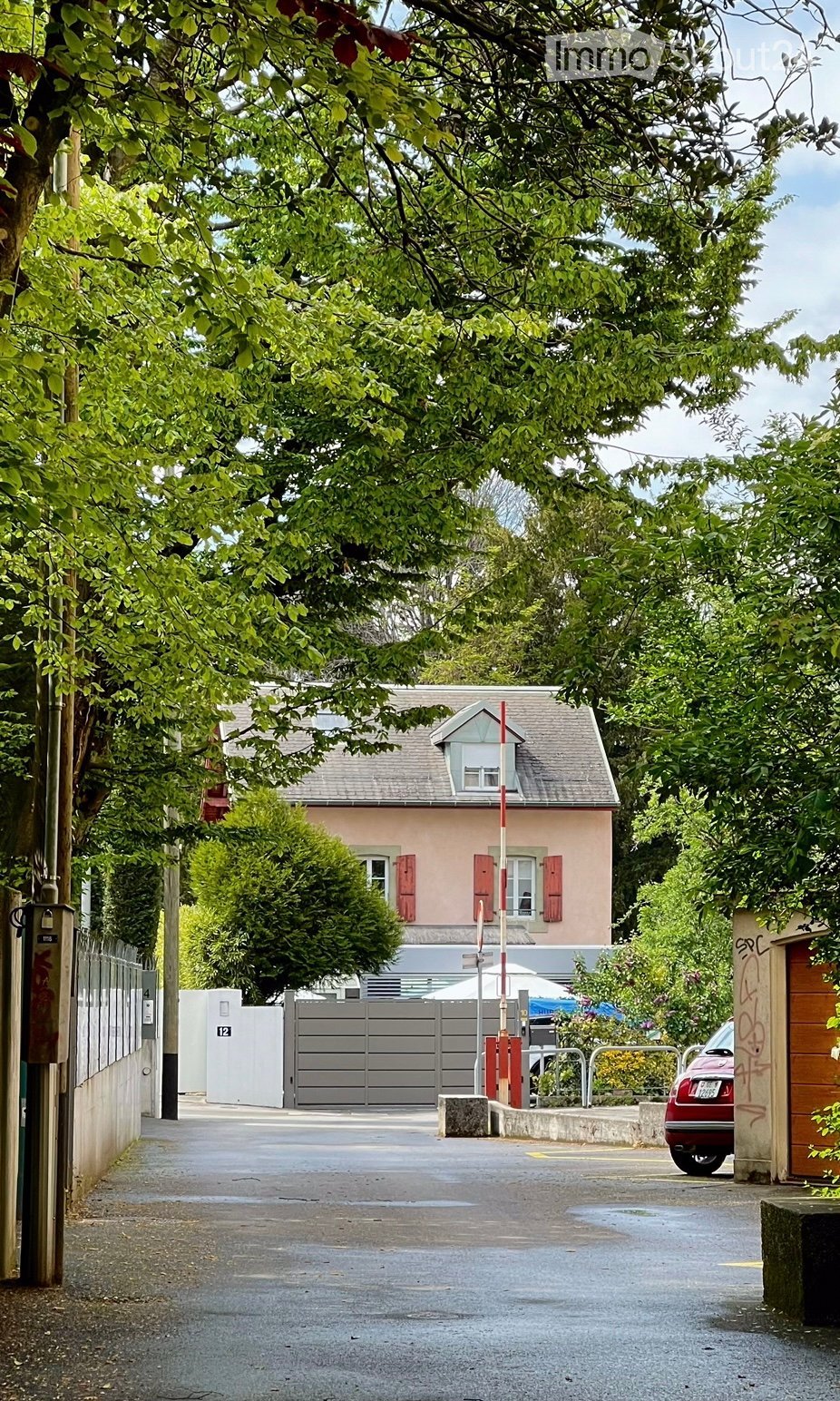 2 story house, pink paint, gray roof, gated entrance, driveway, small garden, grey gate, red car parked