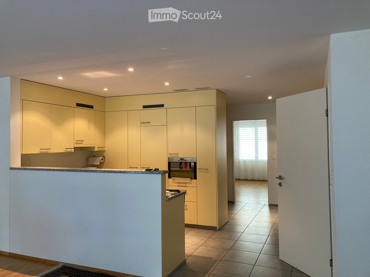 Modern kitchen with light-colored cabinets, a built-in oven, and a countertop, featuring tiled flooring and recessed lighting.