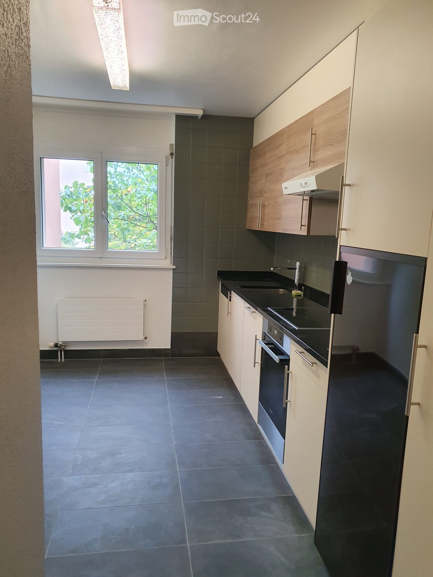 Modern kitchen with white and wood cabinets, black countertops, and stainless steel appliances. Features a window with a view of greenery.