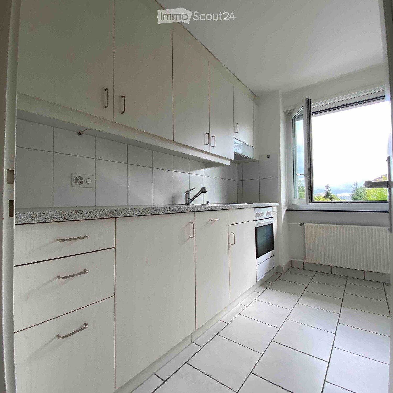 Modern kitchen with white cabinets, tiled backsplash, and a window overlooking a scenic view.