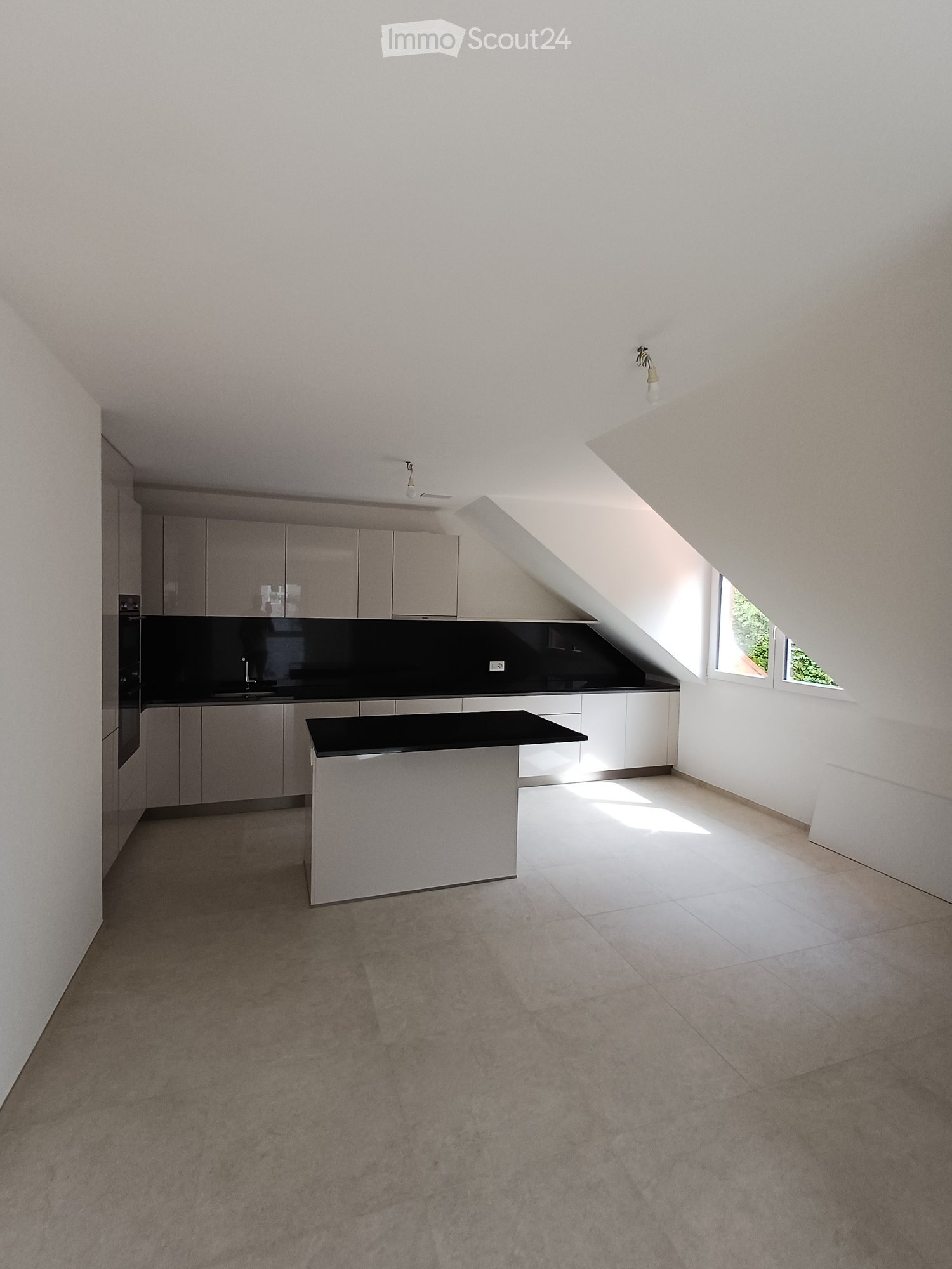 Modern kitchen with white cabinetry, black countertop, central island, and built-in appliances. Natural light from skylight and windows.