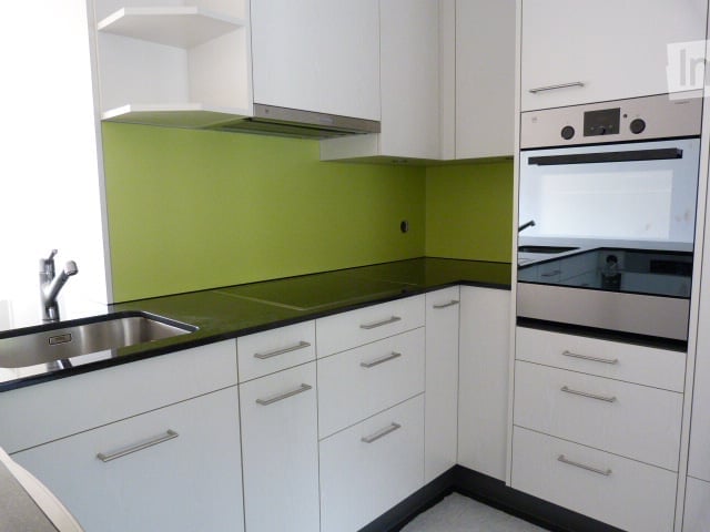 Modern kitchen with white cabinets, green backsplash, black countertops, and stainless steel appliances including a sink and oven.
