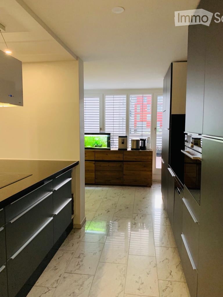 Spacious kitchen with marble tile flooring, black cabinets, wooden drawers, and a dishwasher visible on the counter. Large windows provide natural light and a view of the exterior.