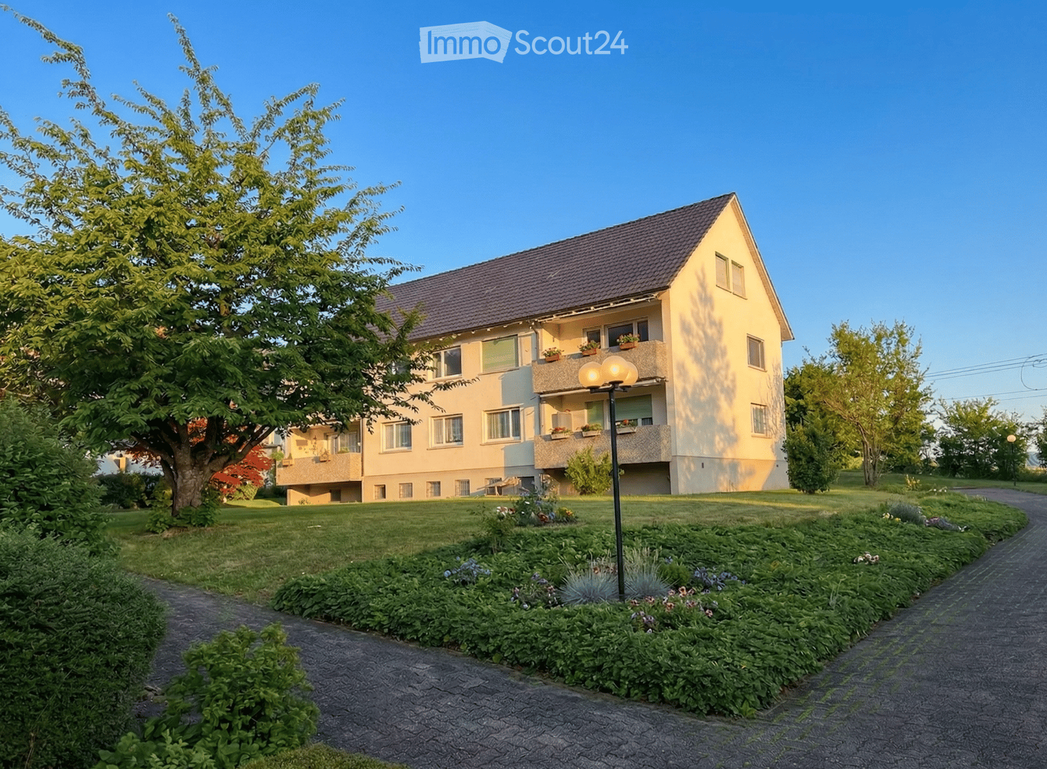 3 story house, beige exterior, multiple balconies, large tree in front, paved walkway, garden