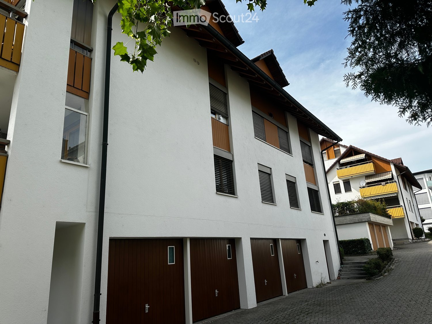 Modern multi-story building with white facade, wooden shutters, and multiple garage doors.