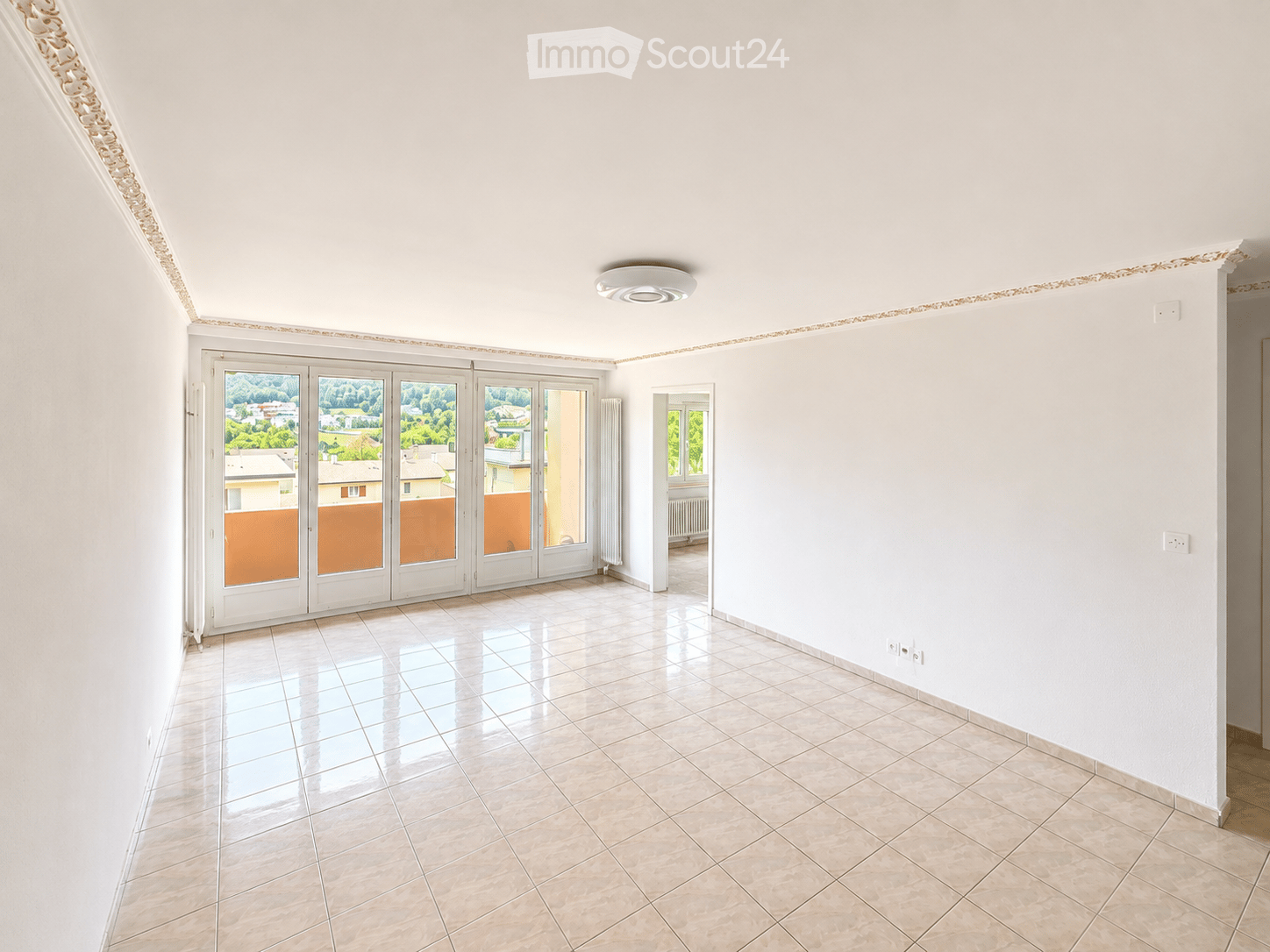 Empty room with white walls, tiled floor, large sliding glass doors leading to a balcony, and a small window on the right side.