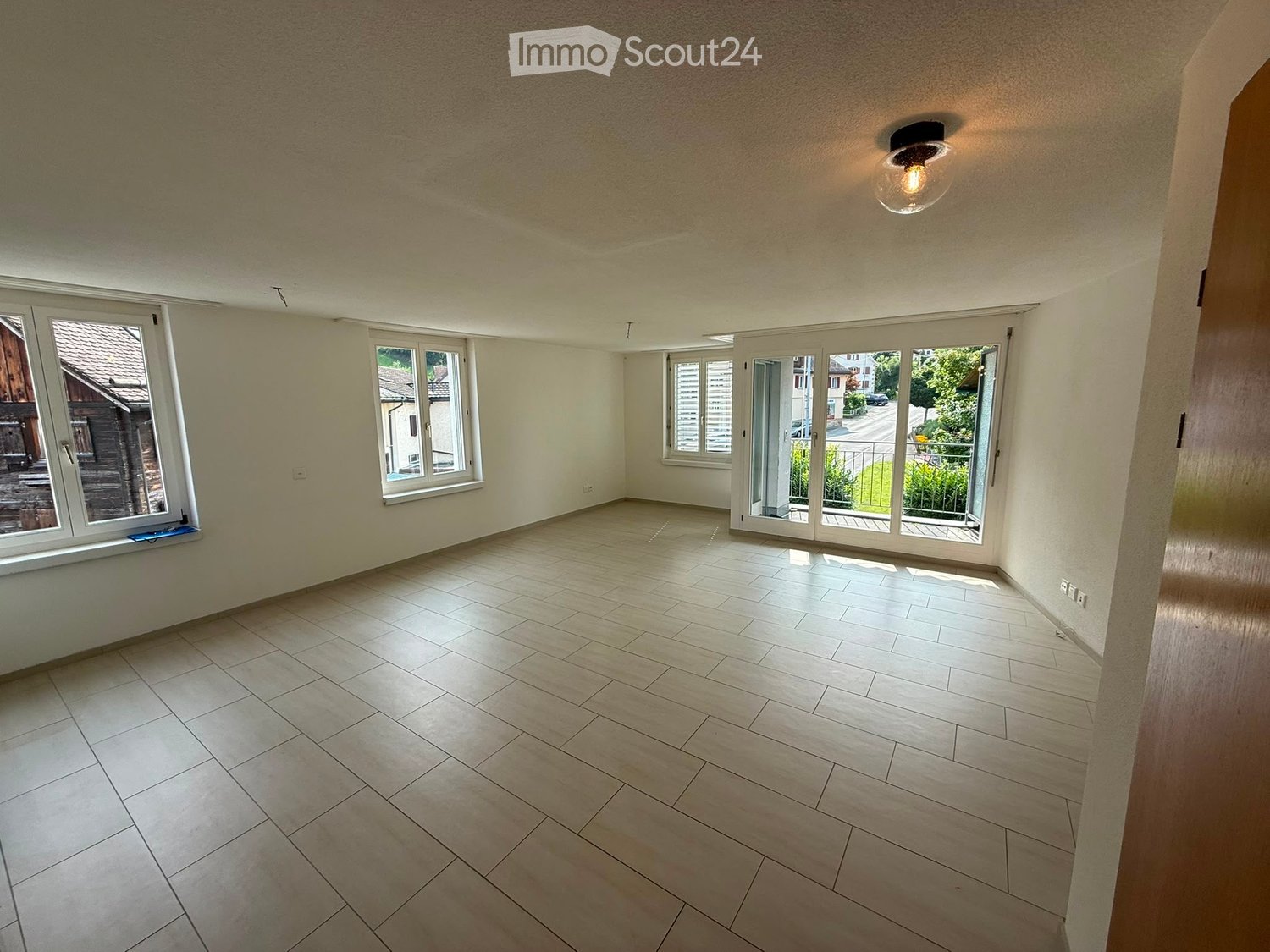 Empty room with tiled floor, large windows, and sliding glass doors leading to a balcony.