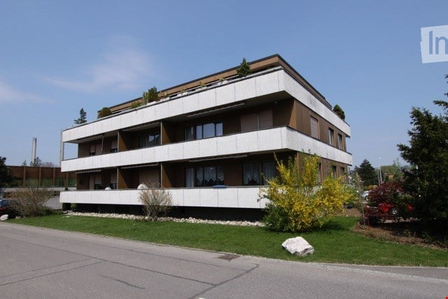 3 story building, white and brown exterior, multiple balconies, windows, green lawn, trees