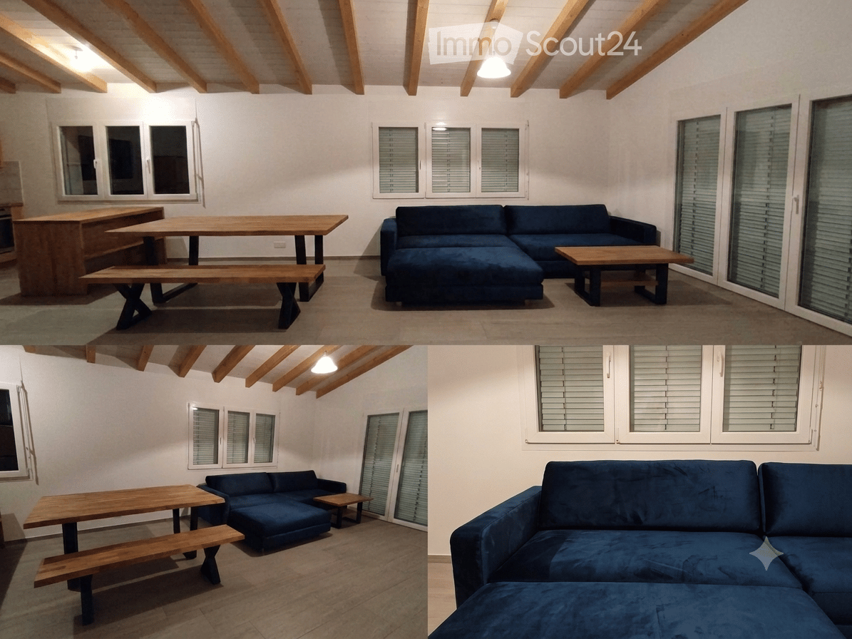 Bright living room with exposed wooden beams, large windows, dark blue sectional sofa, wooden coffee table, dining table with benches.