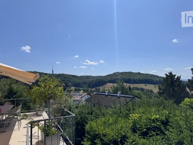 Balcony with a scenic view of a valley, trees, and houses below. Includes a small table and chairs, potted plants, and a railing.