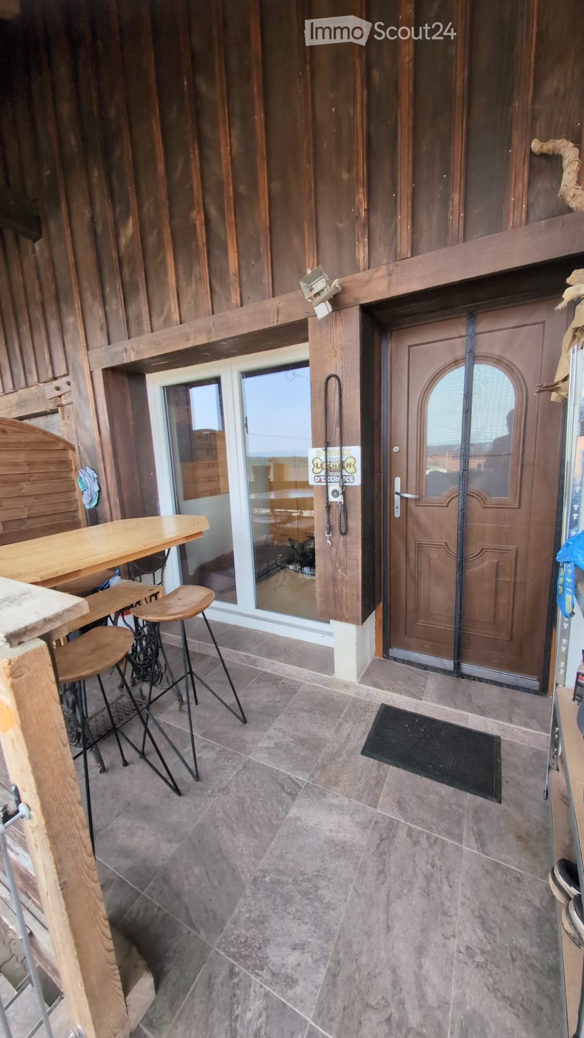 Balcony with wooden table, stools, and a door leading inside.