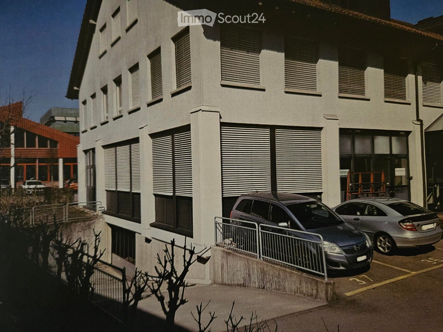 Modern multi-story building with grey facade, large windows, and a parked car in front.