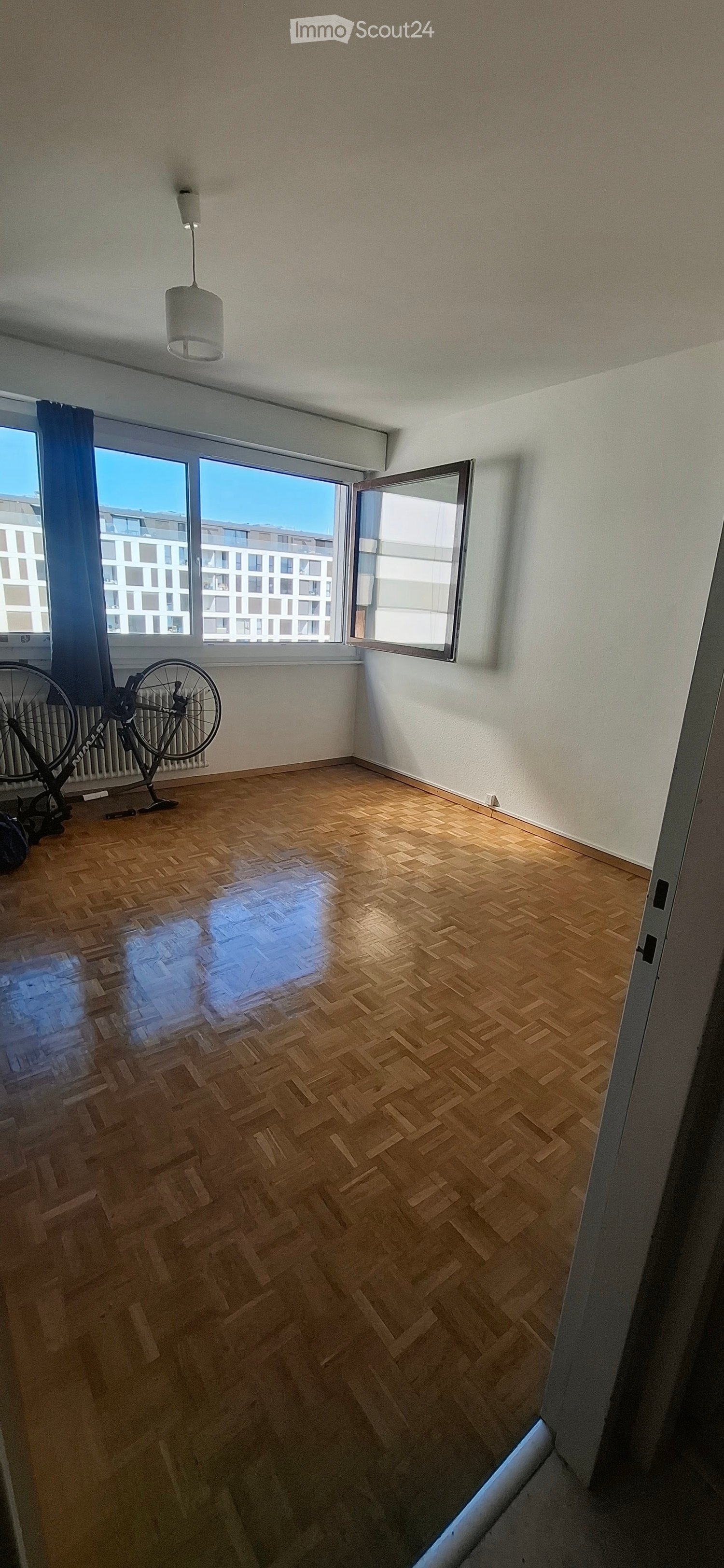 Empty room with wooden parquet flooring, large windows with open shutters, and a bicycle positioned near the wall.