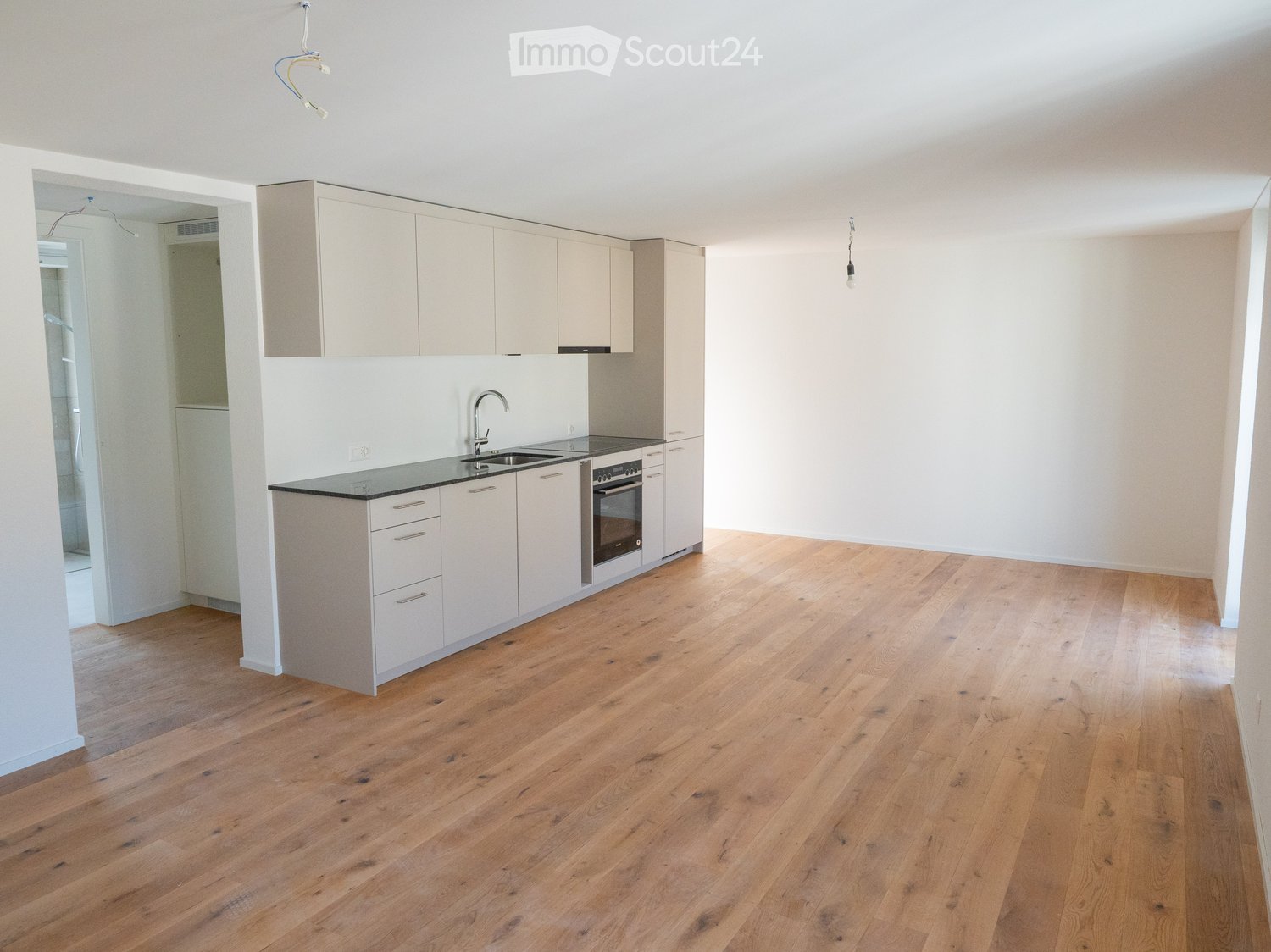 Modern kitchen with light-colored cabinets, a black countertop, and a wooden floor. The kitchen features a sink, oven, and ample storage space.