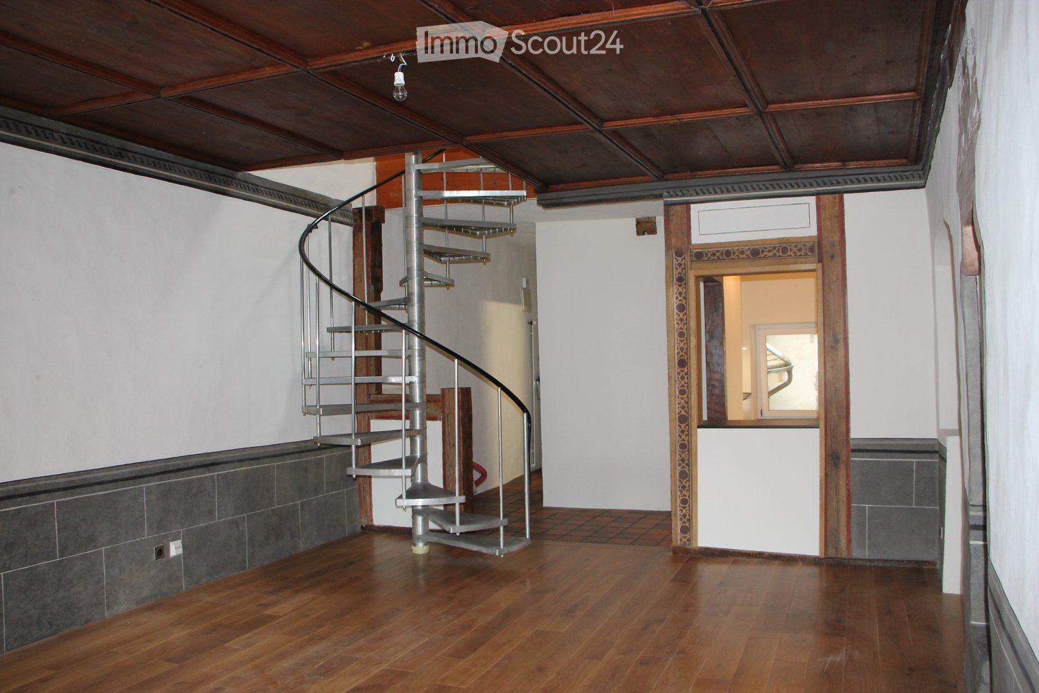 Empty hallway with wooden flooring, white walls, and a modern spiral staircase leading upwards.