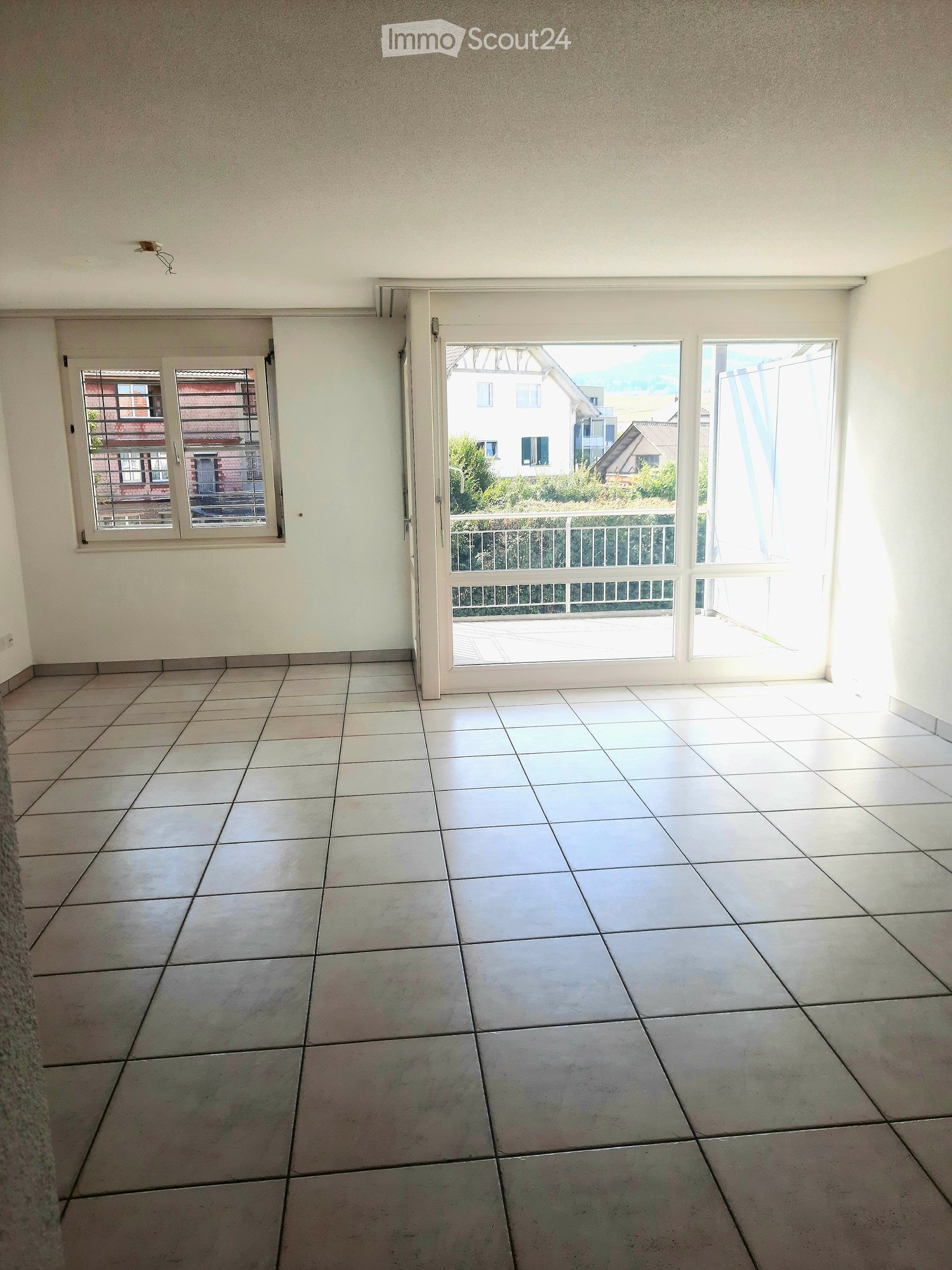 Empty room with tiled floor, white walls, large sliding glass door leading to a balcony, and a window with blinds.