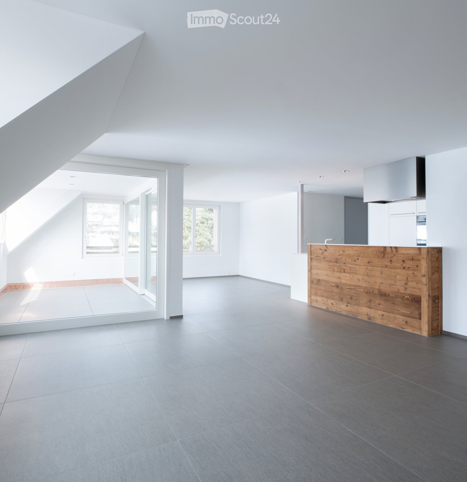 Modern, minimalist kitchen with a wooden counter, white walls, and large windows allowing natural light to fill the space.