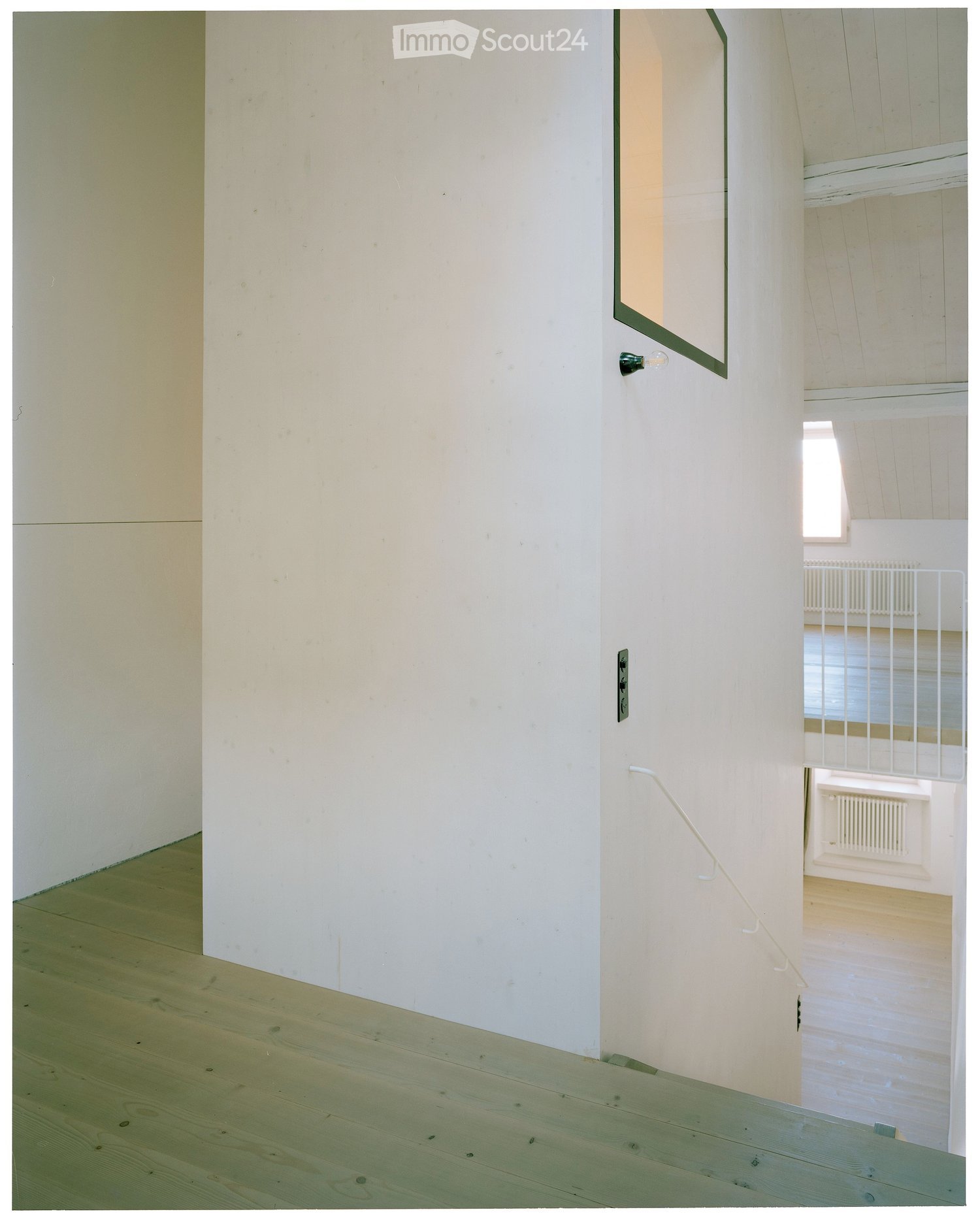Empty hallway with light-colored wooden flooring and white walls, featuring a staircase leading upwards.