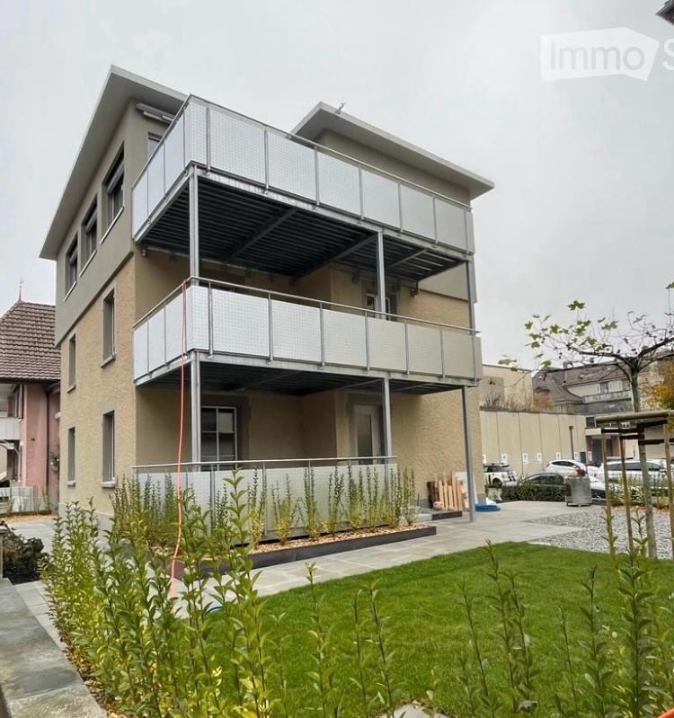 Modern two-story house with balconies, a small garden, and a parking area.