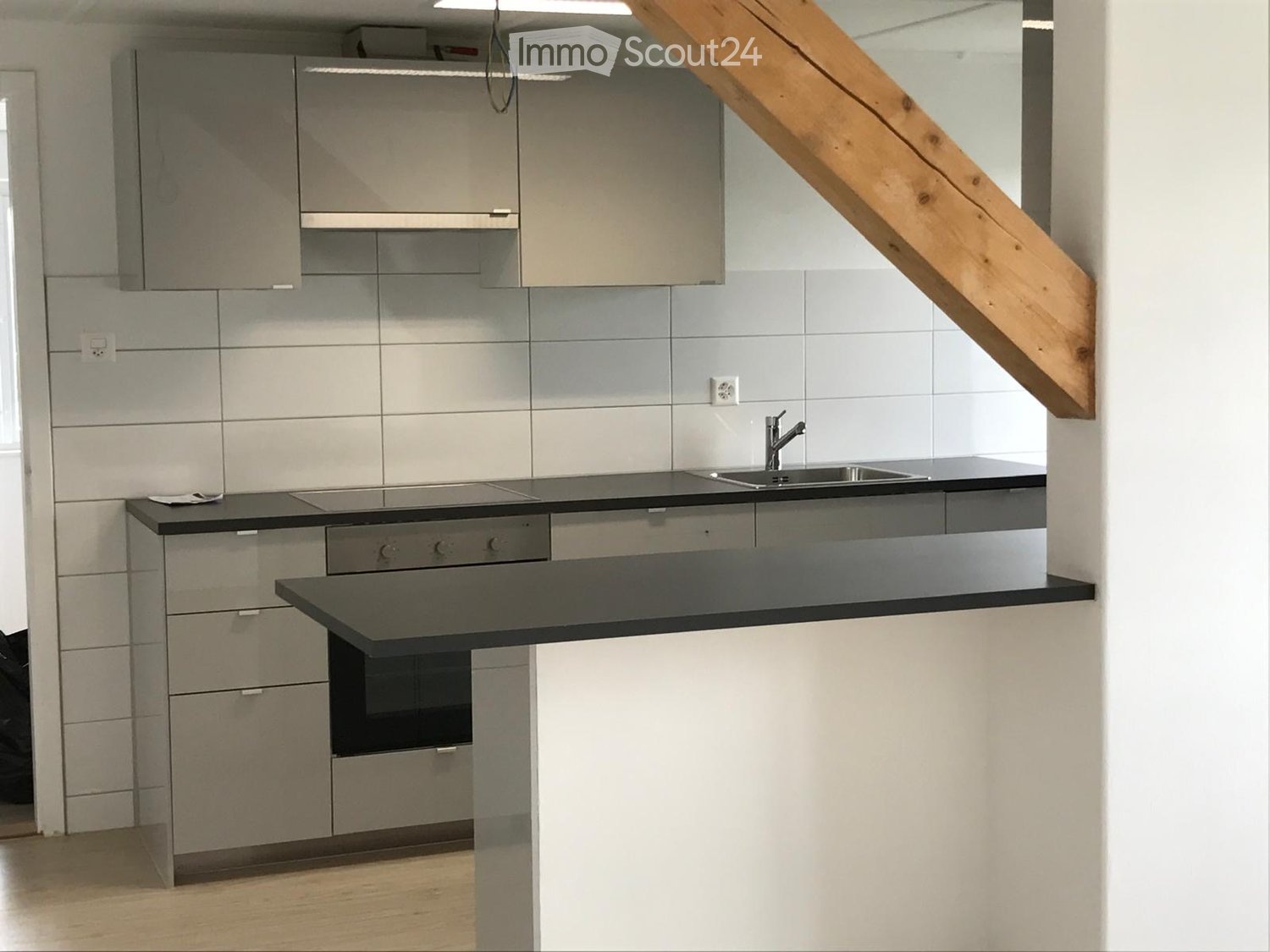 Modern kitchen with grey cabinets, black countertops, stainless steel sink, and built-in oven.