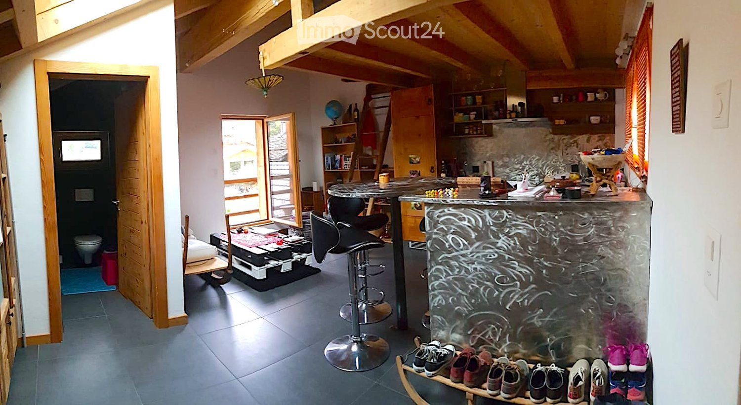 {"visible_features": [], "type": "Living area", "description": "open living area with high wooden ceiling, table, chairs, stools, counter, kitchen and storage shelves, globe, ladder"}