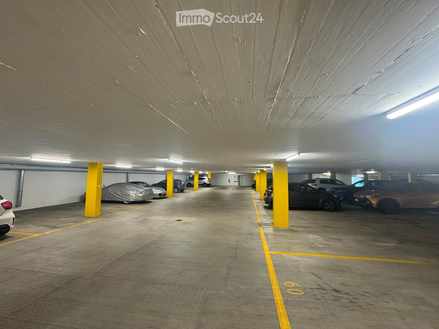 Underground parking area with several parked cars, yellow pillars, and marked parking spaces.