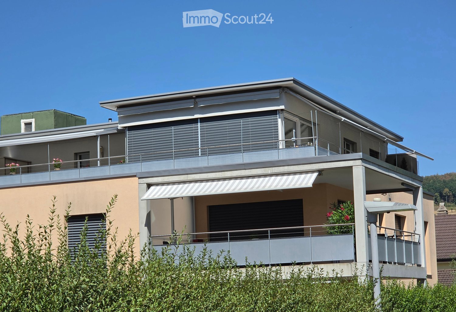 Modern two-story house with beige and green exterior, multiple balconies, and a covered entrance area.