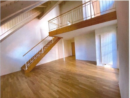 Empty room with wooden flooring, white walls, and a staircase leading to an upper level with a wooden railing.