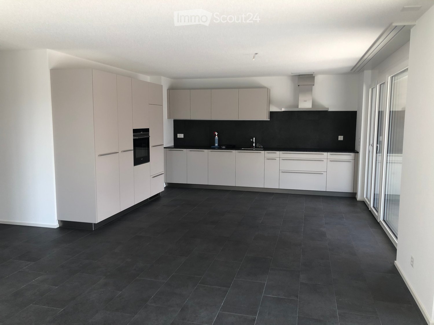 Modern kitchen with white cabinets, black countertop, and dark tiled floor. Features an oven, sink, and faucet.