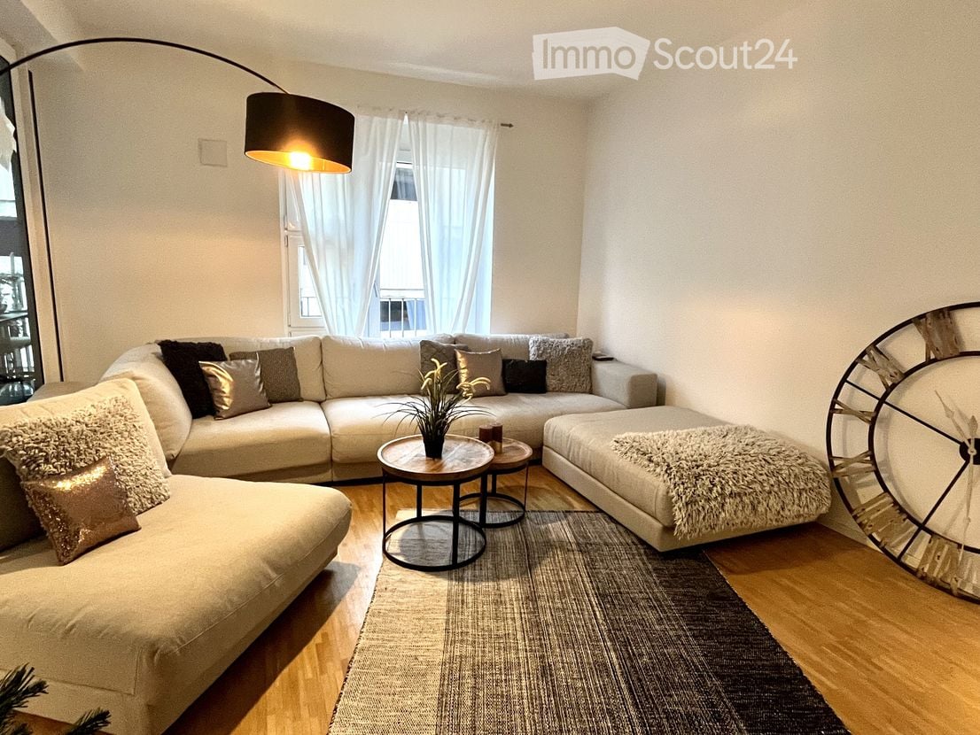Modern living room with a large sectional sofa, multiple throw pillows, a coffee table, a floor lamp, a large mirror, and a small plant on a side table.