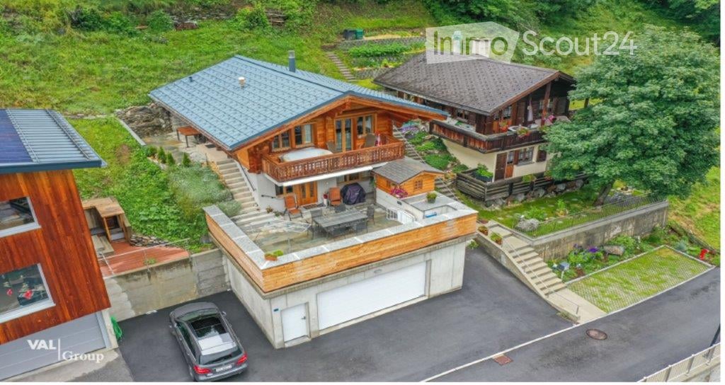 Aerial view of a multi-level house with a garage, parking area, and swimming pool, surrounded by greenery and neighboring houses.