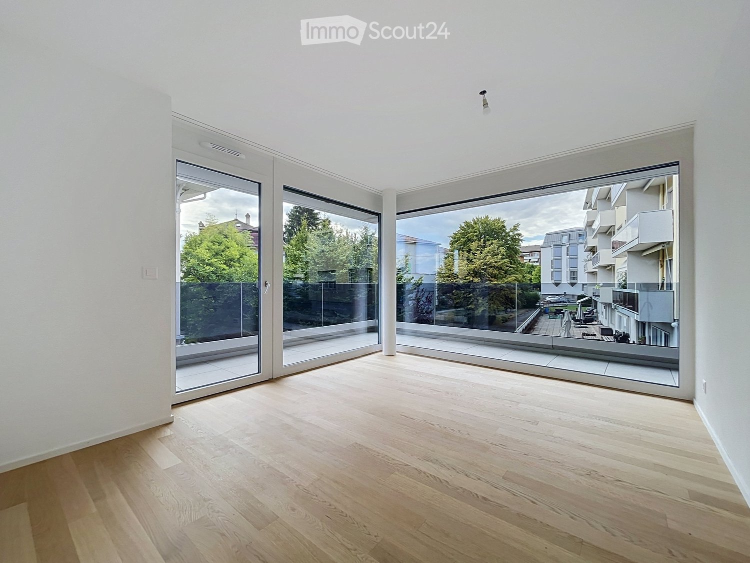 Empty room with light wooden flooring and large glass sliding doors leading to a balcony area with outdoor furniture visible.