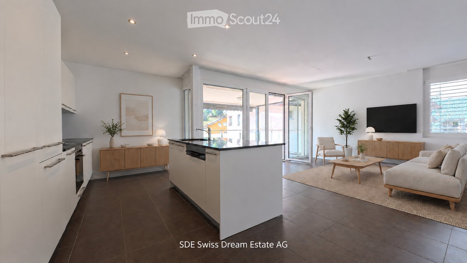 Modern open-plan living and dining area with a kitchen island, sofa, coffee table, armchair, and a television. The space features large windows and sliding glass doors leading to a balcony.