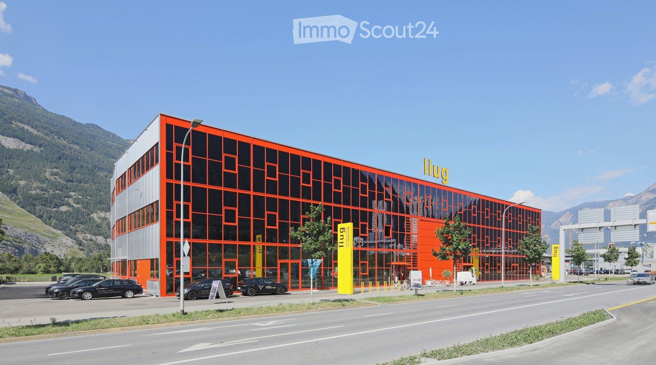 Modern, multi-story building with orange and black facade, large glass windows, and a parking area with several cars.