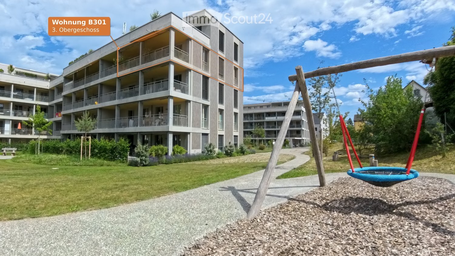 Modern multi-story residential building with balconies, surrounded by a landscaped garden area with a playground featuring a swing and a round nest swing.