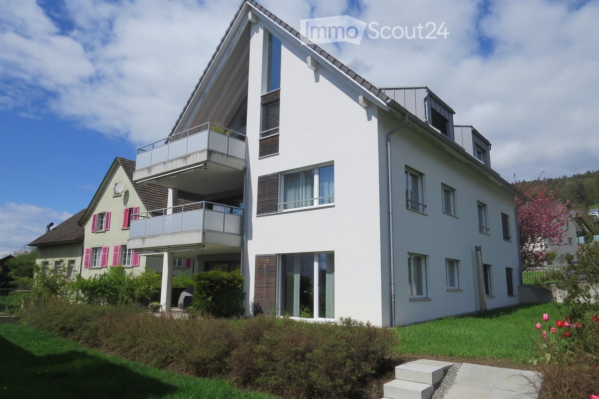 Modern two-story house with white exterior, multiple balconies, large windows, and well-maintained garden.